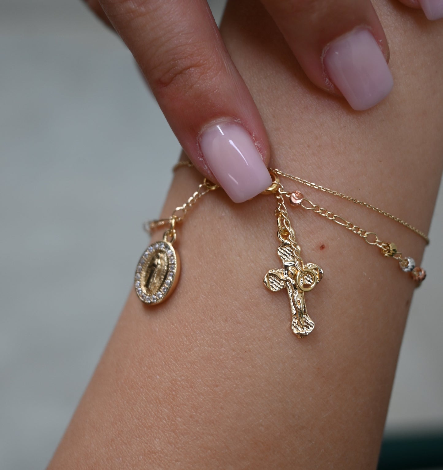 Gold bracelet with charms on a wrist against a neutral background
