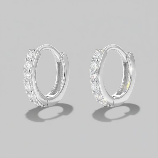 A pair of hoop earrings, with one earring slightly in front of the other, placed on a white, textured surface with a shadow falling across the image.