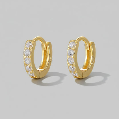 A pair of hoop earrings, with one earring slightly in front of the other, placed on a white, textured surface with a shadow falling across the image.