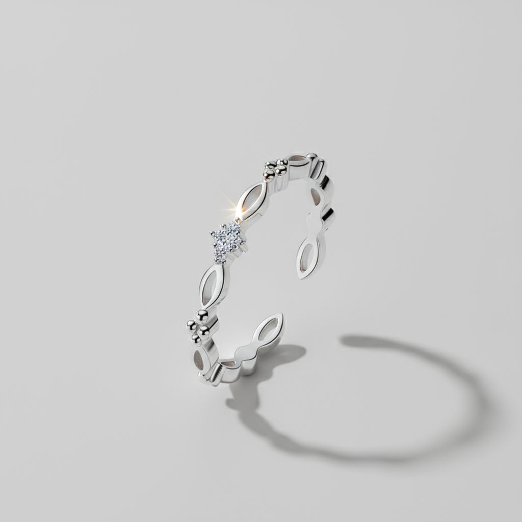 A dainty ring with gold and silver options displayed on a white columnar base with a mirror reflection, set against a silky backdrop.