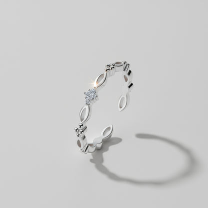 A dainty ring with gold and silver options displayed on a white columnar base with a mirror reflection, set against a silky backdrop.