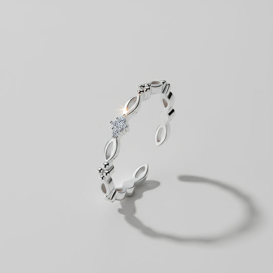 A dainty ring with gold and silver options displayed on a white columnar base with a mirror reflection, set against a silky backdrop.